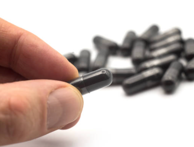 Hand holding a small black cylindrical object with a pile of similar objects in the background.