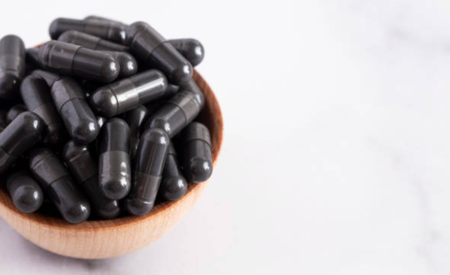 Black capsules in a wooden bowl on a white background